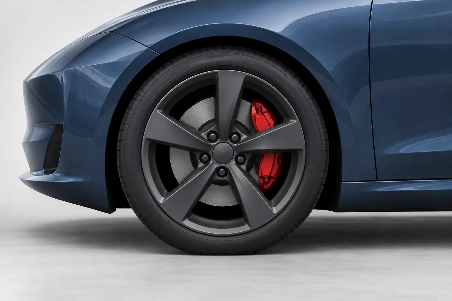 A slate-blue front wing surrounds a dark graphite wheel, with a small red caliper visible behind its spokes.